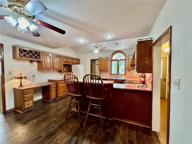 kitchen featuring dark wood finished floors, freestanding refrigerator, built in study area, a textured ceiling, and a peninsula