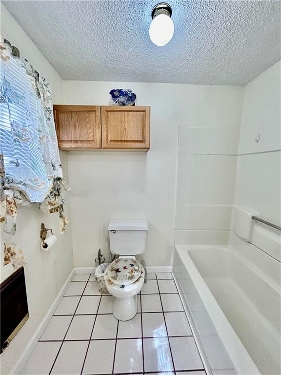 bathroom with a textured ceiling, toilet, and tile patterned floors