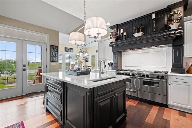 kitchen with sink, dark hardwood / wood-style flooring, an island with sink, range with two ovens, and white cabinets