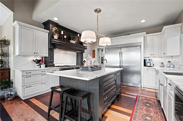 kitchen featuring a kitchen island with sink, hanging light fixtures, dark hardwood / wood-style flooring, decorative backsplash, and white cabinets