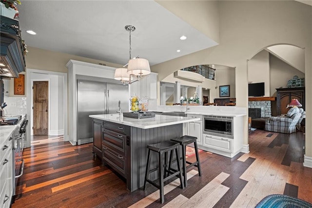 kitchen featuring built in appliances, a kitchen island, a stone fireplace, and white cabinetry