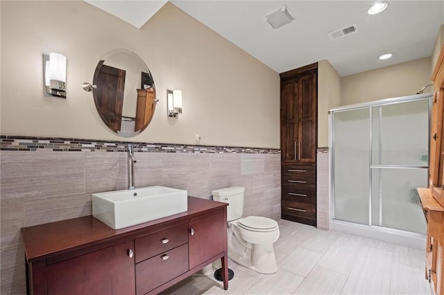 bathroom featuring vanity, toilet, a shower with shower door, and tile walls