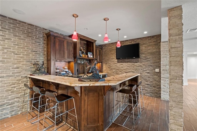 bar featuring dark brown cabinets, pendant lighting, and brick wall