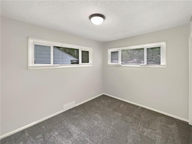 unfurnished room featuring a textured ceiling and dark carpet