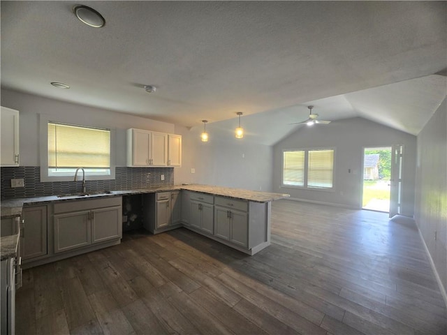 kitchen featuring dark wood-type flooring, sink, hanging light fixtures, kitchen peninsula, and backsplash