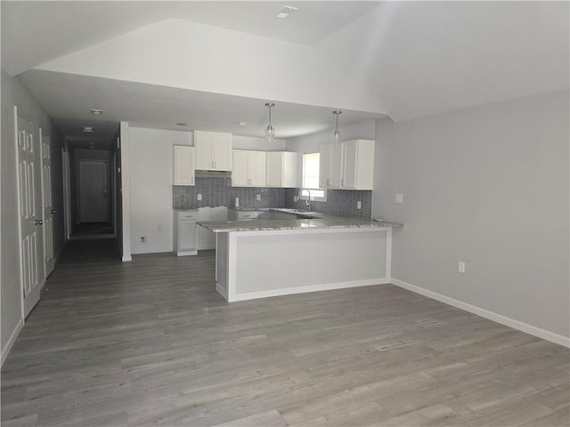 kitchen with lofted ceiling, white cabinets, decorative backsplash, kitchen peninsula, and light wood-type flooring