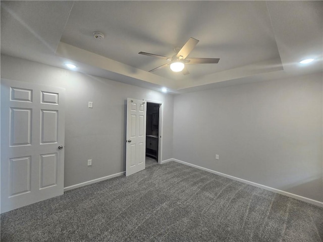 unfurnished bedroom featuring dark carpet, a tray ceiling, and ceiling fan