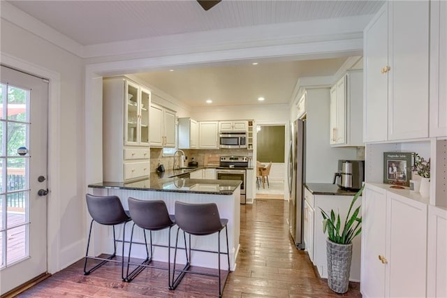 kitchen with sink, appliances with stainless steel finishes, white cabinetry, dark hardwood / wood-style flooring, and kitchen peninsula