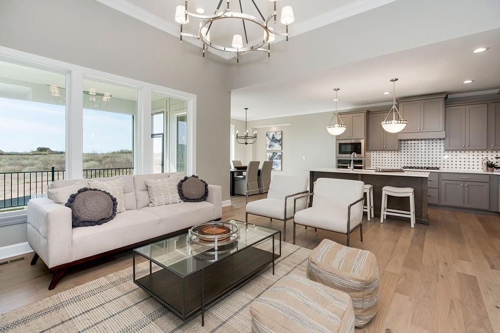 living area with a chandelier, light wood-type flooring, visible vents, and crown molding