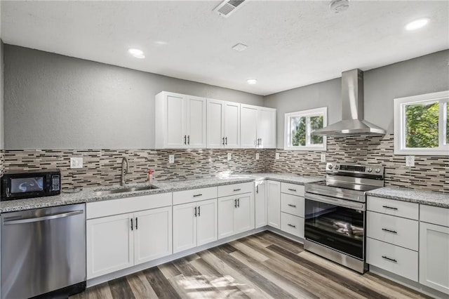 kitchen featuring sink, wall chimney range hood, white cabinetry, hardwood / wood-style flooring, and stainless steel appliances