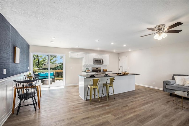 kitchen with hardwood / wood-style floors, white cabinetry, a kitchen bar, stainless steel appliances, and ceiling fan