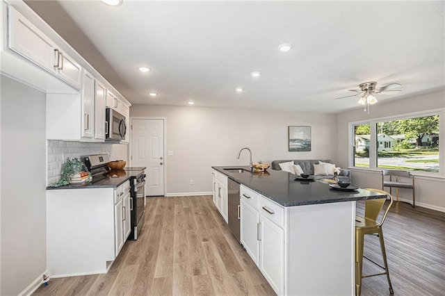 kitchen with white cabinets, appliances with stainless steel finishes, sink, ceiling fan, and a center island with sink