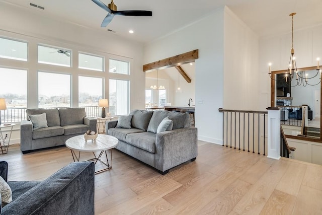 living room with ceiling fan with notable chandelier, high vaulted ceiling, plenty of natural light, and light hardwood / wood-style flooring