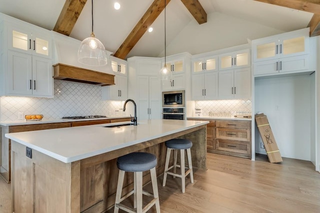 kitchen with appliances with stainless steel finishes, hanging light fixtures, white cabinets, sink, and a large island with sink