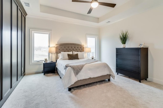 bedroom with a raised ceiling, ceiling fan, and light colored carpet