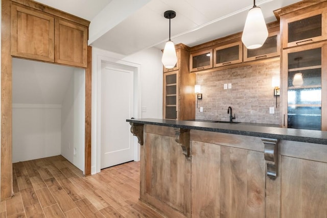 bar featuring hanging light fixtures, light hardwood / wood-style floors, sink, and backsplash