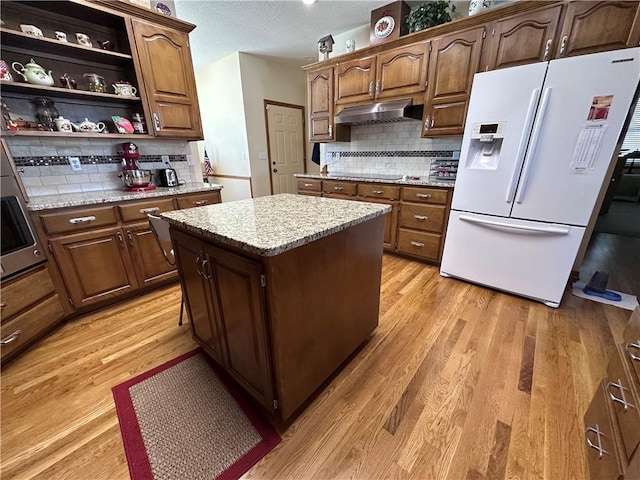 kitchen with a center island, white fridge with ice dispenser, decorative backsplash, and wood-type flooring