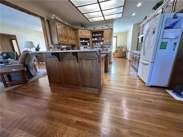 kitchen with white fridge, a kitchen bar, dark hardwood / wood-style floors, kitchen peninsula, and light stone countertops