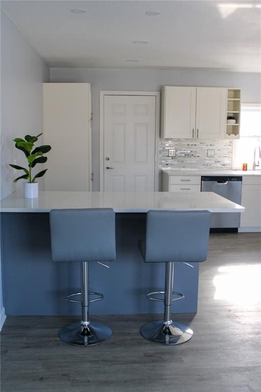 kitchen featuring dishwasher, white cabinetry, decorative backsplash, kitchen peninsula, and a breakfast bar area