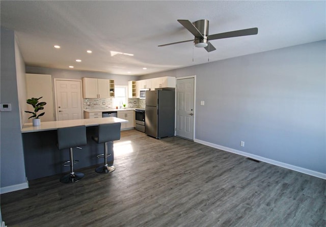 kitchen featuring backsplash, a breakfast bar, white cabinetry, dark wood-type flooring, and appliances with stainless steel finishes