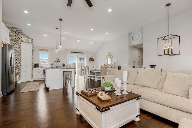 living room with ceiling fan with notable chandelier, dark hardwood / wood-style floors, sink, and vaulted ceiling