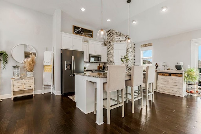 kitchen featuring dark wood-type flooring, stainless steel appliances, an island with sink, and a breakfast bar