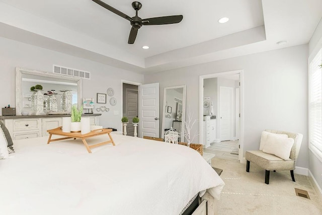 bedroom featuring ceiling fan, ensuite bath, and a tray ceiling