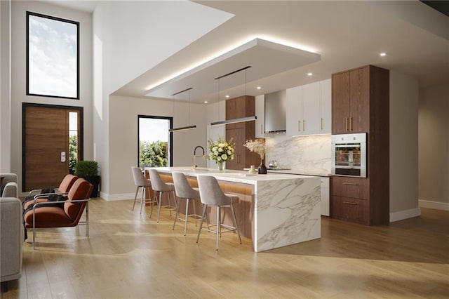 kitchen featuring decorative backsplash, oven, baseboards, modern cabinets, and a large island with sink