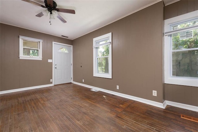 foyer entrance with dark wood-type flooring, ceiling fan, wooden walls, and a healthy amount of sunlight