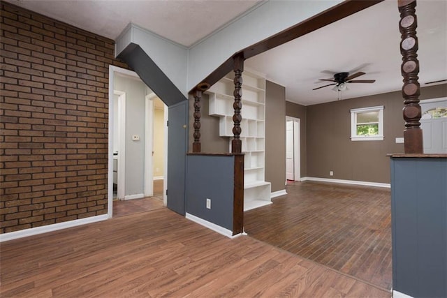 unfurnished living room with wood-type flooring, brick wall, and ceiling fan