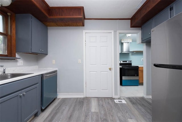 kitchen featuring light wood-type flooring, sink, blue cabinets, appliances with stainless steel finishes, and wall chimney range hood