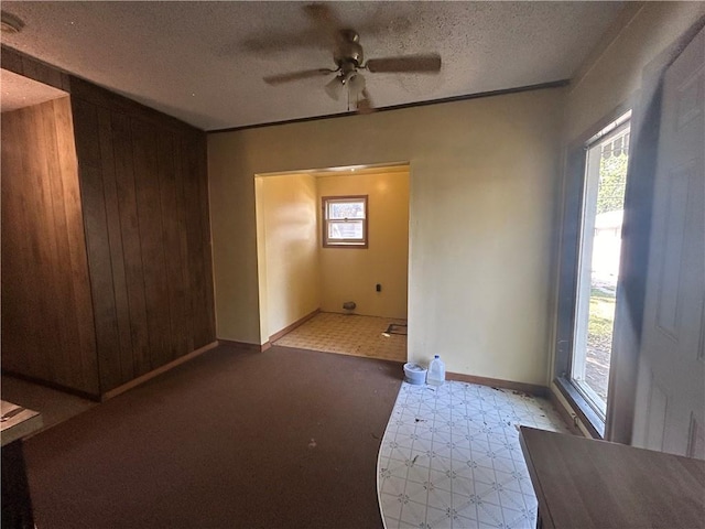 unfurnished room with a textured ceiling, wood walls, and ceiling fan