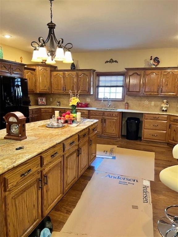 kitchen with black refrigerator, dark wood-type flooring, decorative light fixtures, and sink