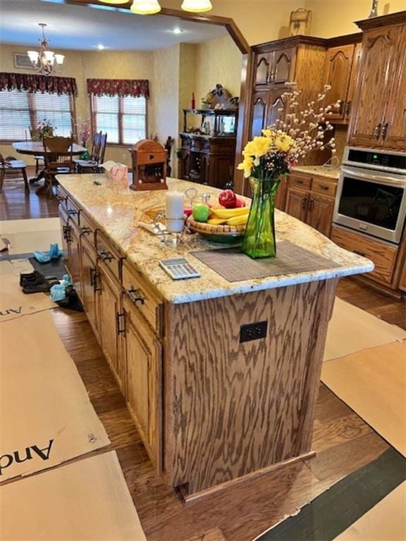 kitchen with oven, light stone counters, a kitchen island, dark hardwood / wood-style flooring, and a chandelier