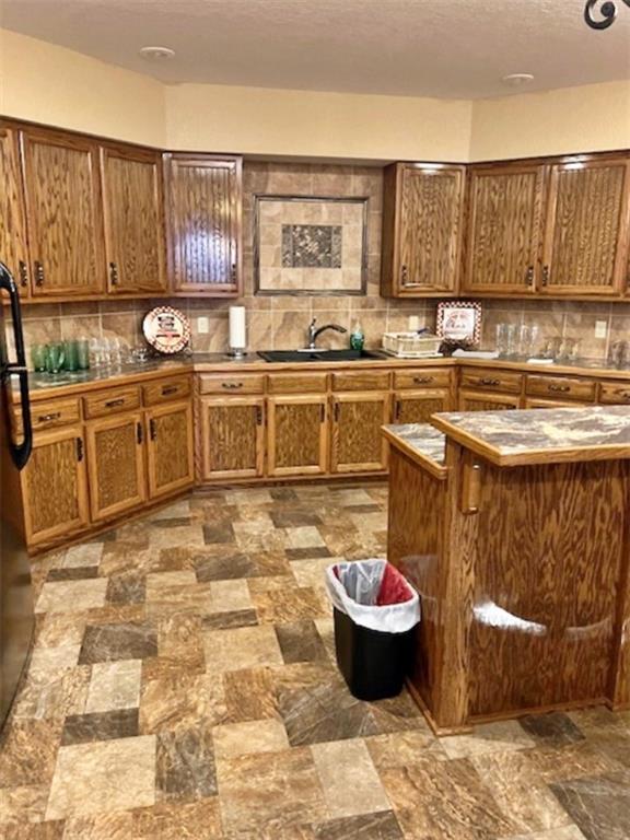 kitchen with backsplash, black refrigerator, and sink