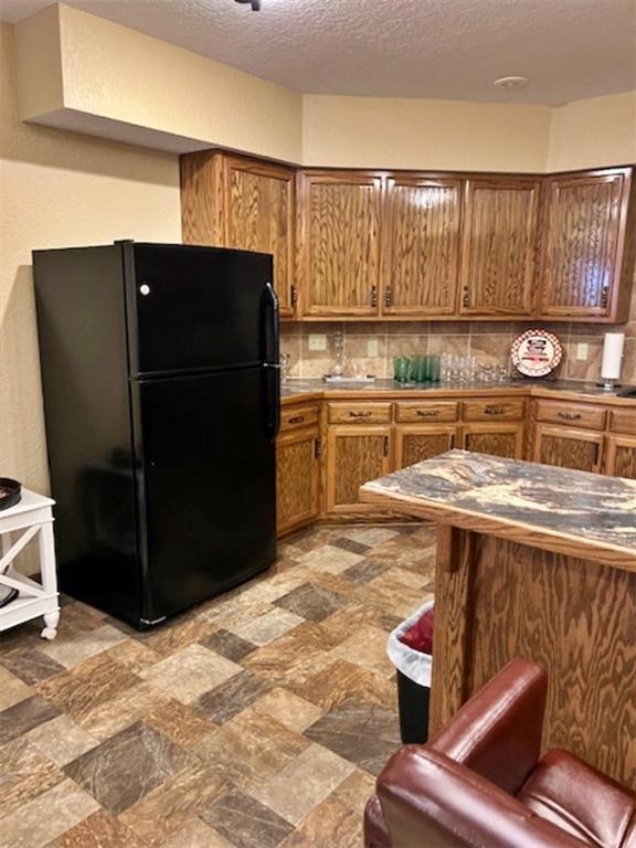 kitchen featuring a textured ceiling, black refrigerator, and backsplash