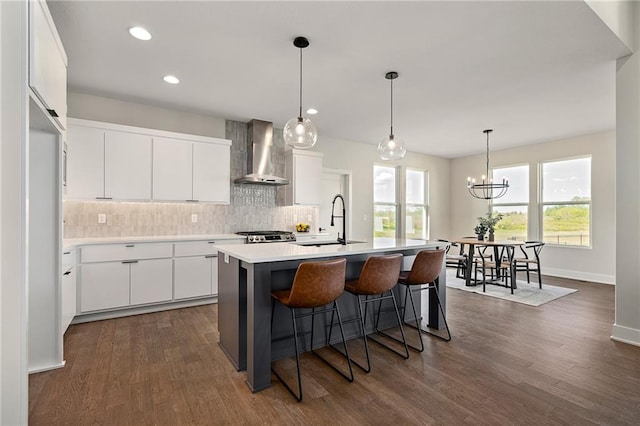 kitchen featuring sink, a center island with sink, wall chimney exhaust hood, white cabinetry, and dark hardwood / wood-style flooring