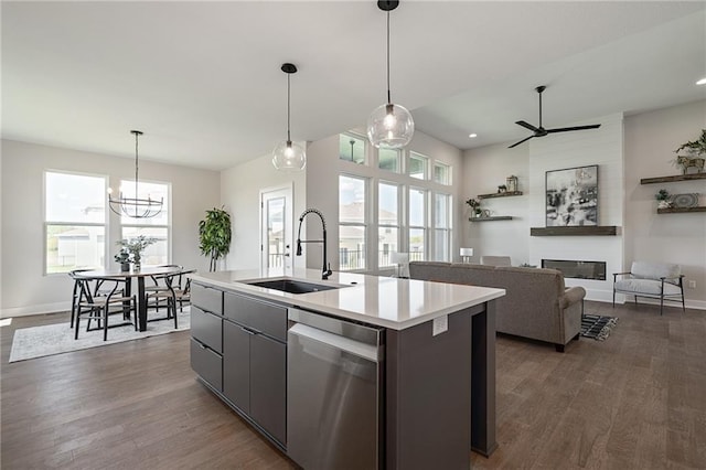 kitchen featuring an island with sink, dark wood-type flooring, dishwasher, a fireplace, and ceiling fan with notable chandelier