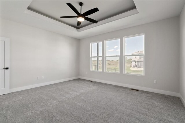 spare room with a tray ceiling, light carpet, and ceiling fan