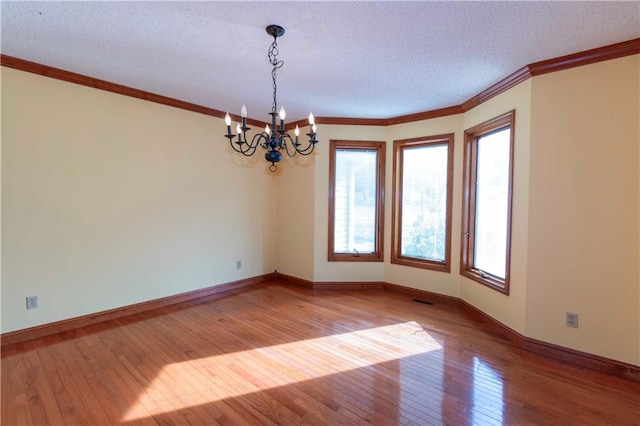 empty room featuring a chandelier, light hardwood / wood-style flooring, and a textured ceiling