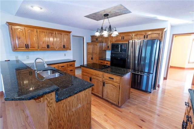 kitchen with a kitchen island, light wood-type flooring, black appliances, a notable chandelier, and sink