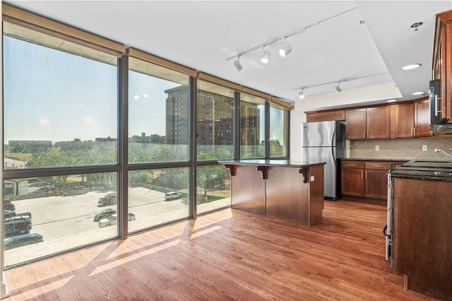 kitchen with a breakfast bar area, a kitchen island, backsplash, hardwood / wood-style flooring, and stainless steel refrigerator