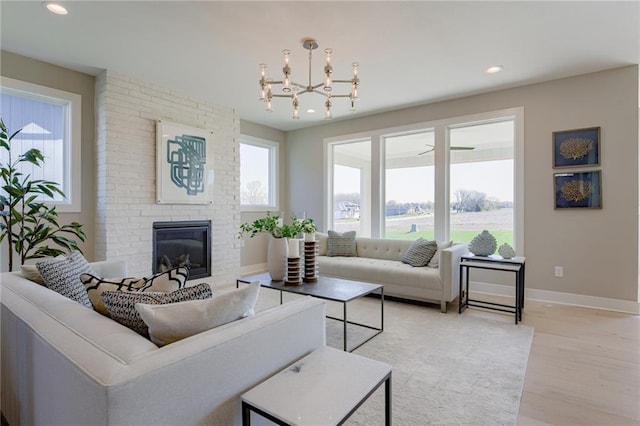 living room featuring plenty of natural light, an inviting chandelier, light hardwood / wood-style flooring, and a brick fireplace