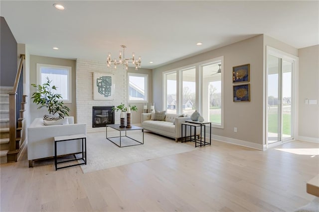 living room with light hardwood / wood-style flooring, ceiling fan with notable chandelier, and a fireplace