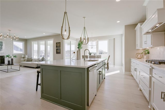 kitchen with an island with sink, sink, custom range hood, and a healthy amount of sunlight