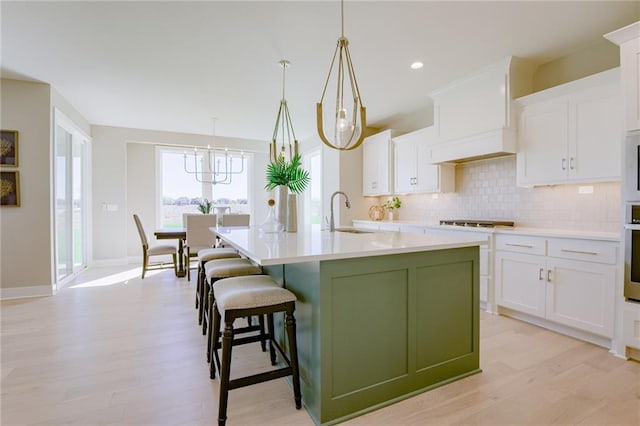 kitchen featuring decorative light fixtures, light hardwood / wood-style floors, an island with sink, sink, and white cabinets