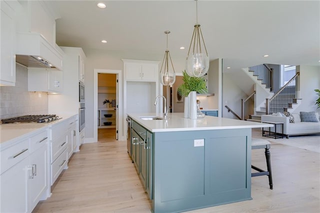 kitchen with light wood-type flooring, an island with sink, sink, hanging light fixtures, and white cabinets