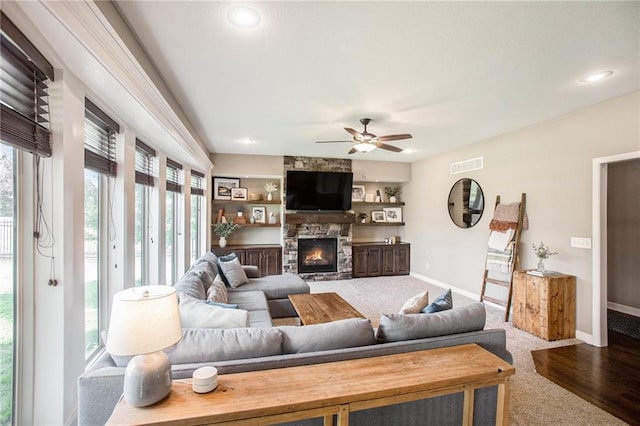 carpeted living room with a stone fireplace and ceiling fan