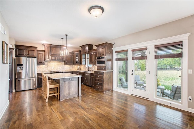 kitchen with a center island, tasteful backsplash, hanging light fixtures, stainless steel appliances, and dark hardwood / wood-style flooring