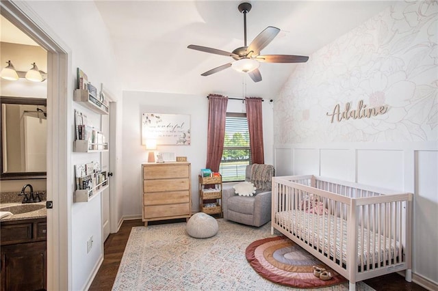 bedroom featuring a crib, dark hardwood / wood-style floors, vaulted ceiling, and ceiling fan